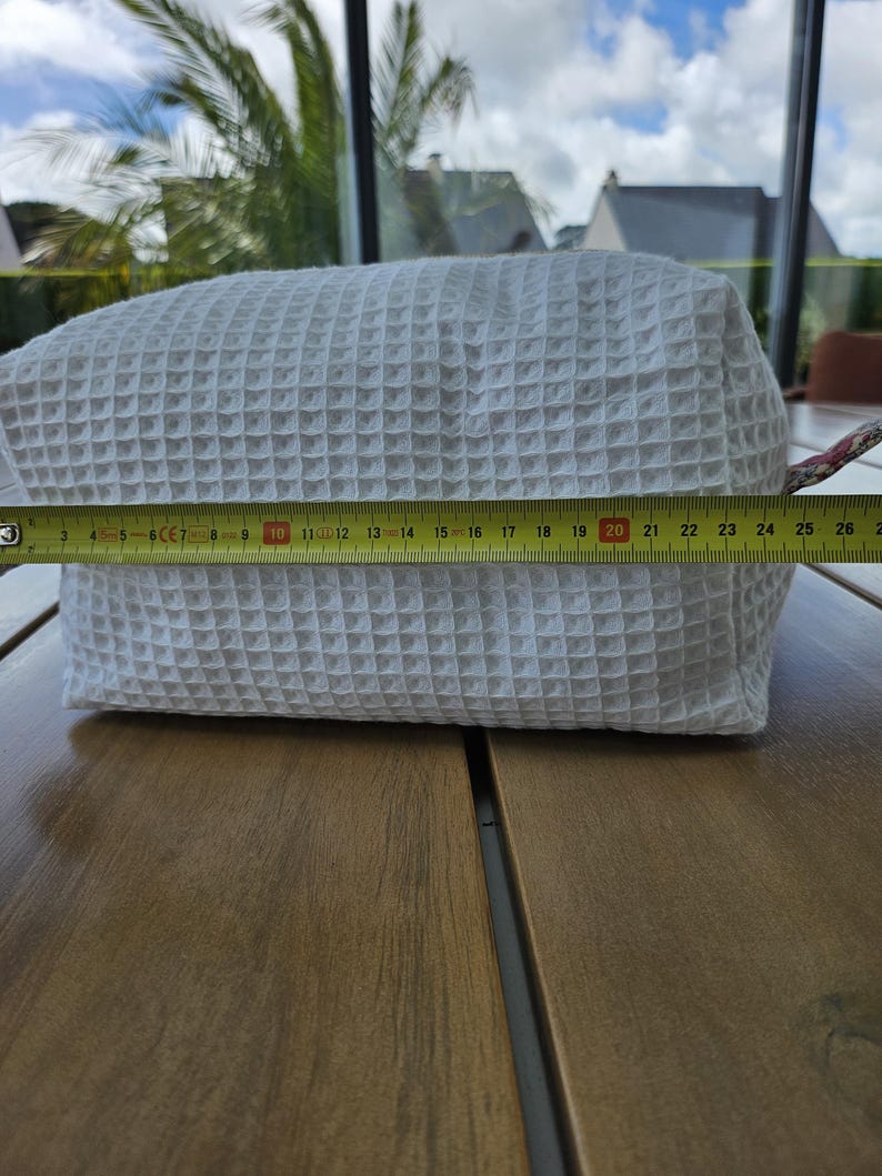 May include: A white rectangular pouch with a textured waffle-weave pattern. A yellow measuring tape is positioned across the front, indicating a length of approximately 10.25 inches from the left edge to the right side of the fabric pouch.