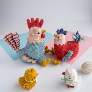 May include: A set of four crocheted yarn figures including a large blue rooster with a red comb, a smaller red hen with a blue comb, a yellow chick, a white chick with a green scarf, and a small white crocheted egg, all featuring stitched details.
