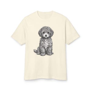 May include: Cream-colored t-shirt featuring a detailed pencil sketch of a seated poodle. The poodle has curly fur and a sweet expression. The t-shirt is a classic crew neck style.