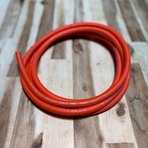 May include: Coiled orange welding cable. The cable is labeled with text including "#2 ULTRA-FLEX WELDING CABLE 600V -50C 31050C". The cable is made in Hong Kong and meets SAE J1127 standards.