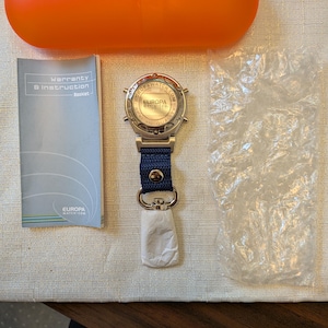 Pode incluir: Um rel&oacute;gio Europa Water prateado com uma bracelete azul marinho e um fecho prateado. O rel&oacute;gio &eacute; acompanhado por um livreto de garantia, uma caixa laranja e uma embalagem pequena. O mostrador do rel&oacute;gio apresenta o texto "EUROPA WATER.COM" e "SEAL THE QUALITY".