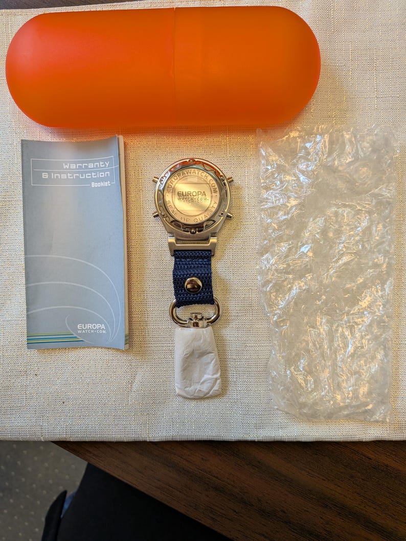 Pode incluir: Um rel&oacute;gio Europa Water prateado com uma bracelete azul marinho e um fecho prateado. O rel&oacute;gio &eacute; acompanhado por um livreto de garantia, uma caixa laranja e uma embalagem pequena. O mostrador do rel&oacute;gio apresenta o texto "EUROPA WATER.COM" e "SEAL THE QUALITY".