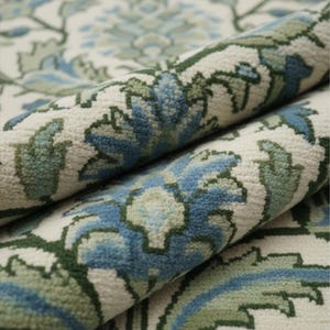 May include: Rolled-up area rug with a floral pattern in shades of blue, green, and cream. The rug's design features stylized flowers and leaves, creating a textured, decorative surface. The close-up view highlights the detailed weave and color variations.