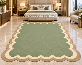 Op de afbeelding: Een rechthoekig vloerkleed met een saliegroen midden, een crèmekleurige geschulpte rand en een buitenste beige geschulpte rand. Het kleed toont de tekst AmbinetRugsCo in het midden. Het ontwerp bestaat uit gelaagde, afgeronde vormen.