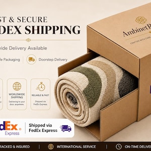 Op de afbeelding: Een opgerold tapijt met een golvend patroon in olijfgroen, beige en donkergrijs, gedeeltelijk in een bruine kartonnen verzenddoos geplaatst met het AmbinetRugsCo-logo en FedEx Express-branding op de zijkant.