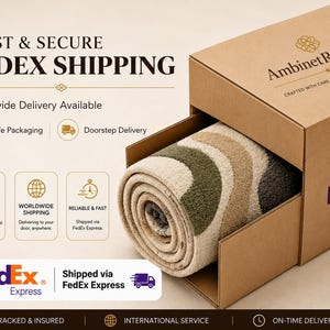 Op de afbeelding: Een opgerold tapijt met een golvend patroon in tinten olijfgroen, beige en donkergrijs, gedeeltelijk in een bruine kartonnen verzenddoos geplaatst met het AmbinetRugsCo-logo en FedEx Express-branding op de zijkant en de voorkant.
