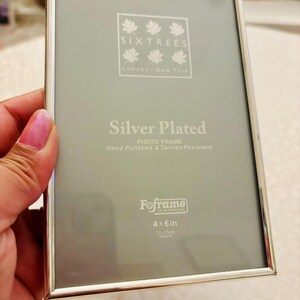 May include: A rectangular silver-plated photo frame with a thin metallic border. The insert displays the text Sixtrees London New York, Silver Plated Photo Frame Hand Polished & Tarnish Resistant, Fofame of Huntingdon, and 4x6 in 10x15cm approx.