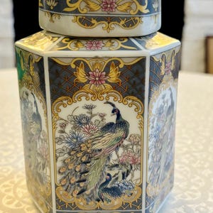 Peut inclure: Un pot à gingembre hexagonal en porcelaine avec couvercle amovible, orné d'un motif détaillé de paon et de fleurs multicolores sur un fond en treillis bleu foncé. Le design inclut des accents dorés, des fleurs roses et du feuillage vert.