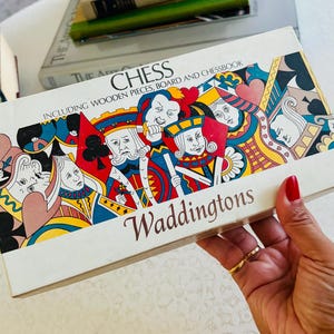 May include: A rectangular Waddingtons chess game box featuring a colorful graphic illustration of playing card characters including kings and queens. The white box displays the text CHESS INCLUDING WOODEN PIECES, BOARD AND CHESSBOOK.