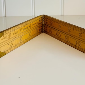 May include: A vintage wooden folding ruler, open in a V-shape. The ruler is marked with inch measurements from 1 to 23. The wood has a warm, aged tone with visible wear. The ruler is a carpentry tool.