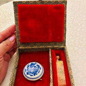 May include: A rectangular box with a patterned fabric exterior and a red velvet interior containing a round white ceramic piece with a blue dragon design and a tall, rectangular stone seal with a carved top and red and gold markings.