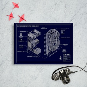 Puede incluir: Una impresión azul marino con planos arquitectónicos de los números 'E8'. El diseño incluye detalles técnicos y texto. Una cámara y grullas de origami se colocan cerca de la impresión.