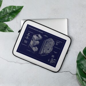 May include: A white laptop sleeve with a black zipper, featuring a blueprint design in navy blue. The blueprint shows the letters "EB" in a 3D architectural style, with technical details and text. The sleeve is on a light surface with green leaves.