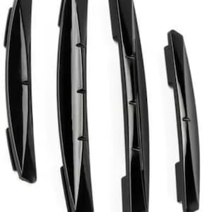 May include: Four black, glossy, curved car door edge guards arranged vertically. Each piece features a sleek, elongated design with a central ridge and a smooth finish. A circular logo in the top right corner displays the text MADE WITH LOVE.