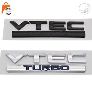 May include: Two VTEC TURBO emblem decals. The top decal is matte black with raised lettering. The bottom decal features a polished chrome finish for the VTEC text and a chrome bar with blue inlay lettering for the word TURBO.
