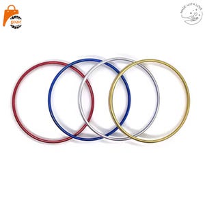 Könnte beinhalten: Vier kreisförmige Metallringe, die in einer horizontalen Reihe angeordnet sind. Die Ringe sind rot, blau, silber und goldfarben. Jeder Ring hat eine glatte, dünne und gleichmäßige röhrenförmige Struktur vor einem weißen Hintergrund.
