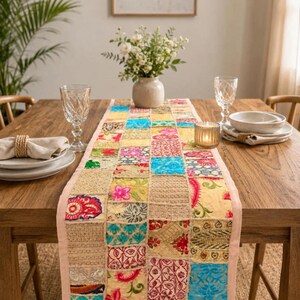 Op de afbeelding: Een rechthoekige tafelloper met een patchworkontwerp van diverse stoffen vierkanten in levendige kleuren zoals blauw, geel, roze en rood. De loper toont diverse bloemen-, paisley- en textuurpatronen met geborduurde details op de stof.