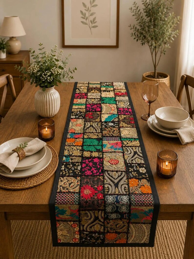 Op de afbeelding: Een rechthoekige tafelloper met een patchworkontwerp van diverse stoffen vierkanten in zwart, roze, groen, oranje en goud. De loper toont ingewikkelde geborduurde bloem- en geometrische patronen met metallic draadaccenten en een zwarte rand.