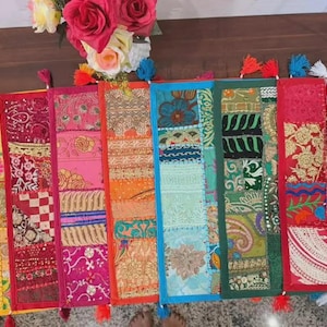 May include: A rectangular table runner featuring a patchwork design of various fabric panels in vibrant colors including yellow, pink, orange, blue, green, and red. The runner is decorated with intricate embroidery, sequins, and small tassels along the edges.