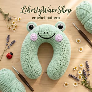 Puede incluir: Una almohada de cuello de ganchillo verde claro con forma de rana, ojos negros, boca bordada negra y mejillas rosas. El texto LibertyWaveShop crochet pattern es visible. Dos ovillos de lana verde claro, dos ganchillos de 6.0mm y flores.