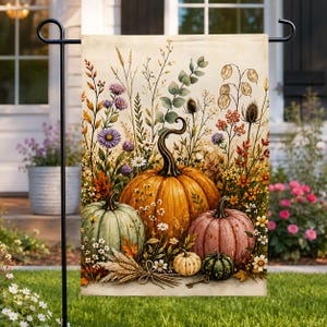 May include: A rectangular garden flag featuring a vibrant illustration of three large pumpkins in orange, sage green, and muted pink, surrounded by a variety of wildflowers, dried grasses, eucalyptus sprigs, and small decorative pumpkins.