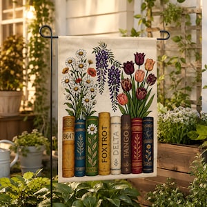 May include: A rectangular garden flag featuring a row of seven vintage-style book spines at the bottom, with colorful flowers including daisies, wisteria, and tulips emerging from the top. The books are labeled with text including 8647, FOXTROT, DELTA, and TANGO.