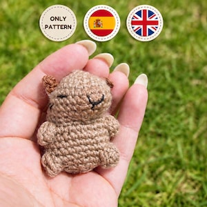 Puede incluir: Una pequeña figura animal de ganchillo en color marrón claro con una cabeza redondeada, dos orejas pequeñas y detalles bordados con hilo negro para los ojos y la boca. El artículo está hecho de hilo y presenta un patrón de punto texturizado.