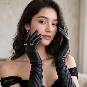 May include: A pair of long black leather gloves reaching past the wrists, featuring a smooth texture and fitted design. The gloves are worn on the hands, which are positioned near the face. The material appears soft and flexible with subtle folds.