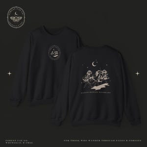 Può includere: Una felpa nera a girocollo con un piccolo logo circolare sul petto e una grande grafica sul retro. Il design posteriore raffigura tre figure che danzano sotto una luna crescente e stelle con il testo DANCING BETWEEN DAYDREAMS.