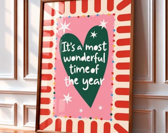 May include: A framed rectangular wall art print featuring a large dark green heart on a pink background. The text It's a most wonderful time of the year is written in white. The border has red rounded stripes and colorful dots.