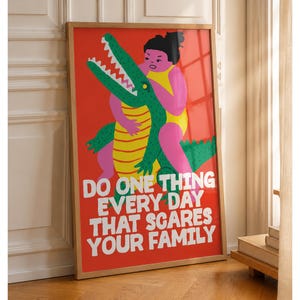 Puede incluir: Un p&oacute;ster rectangular enmarcado con fondo rojo brillante que presenta una ilustraci&oacute;n gr&aacute;fica de una persona en traje de ba&ntilde;o amarillo abrazando a un cocodrilo verde con vientre a rayas amarillas. El texto blanco dice: DO ONE THING EVERY DAY THAT SCARES YOUR FAMILY.