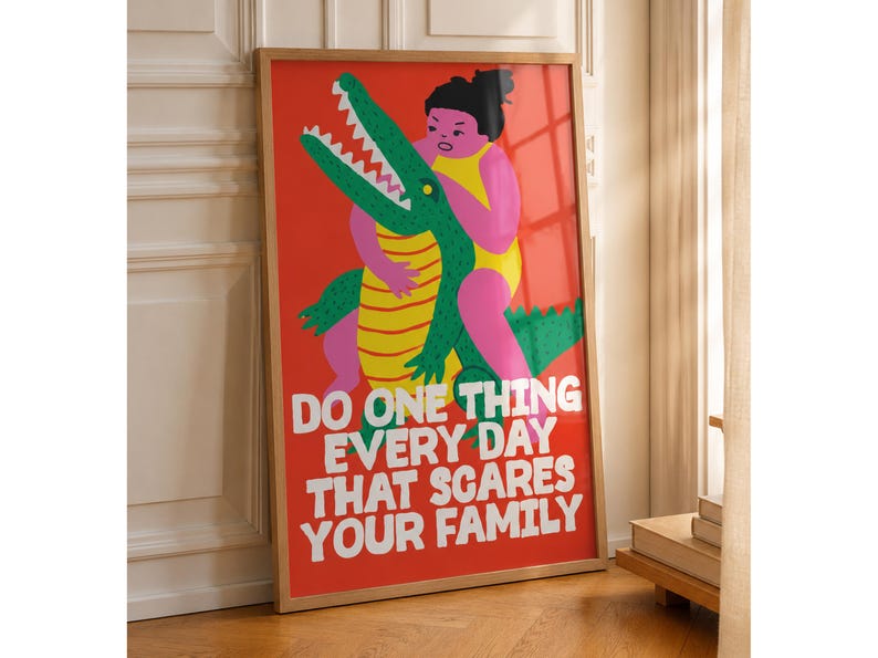 Puede incluir: Un p&oacute;ster rectangular enmarcado con fondo rojo brillante que presenta una ilustraci&oacute;n gr&aacute;fica de una persona en traje de ba&ntilde;o amarillo abrazando a un cocodrilo verde con vientre a rayas amarillas. El texto blanco dice: DO ONE THING EVERY DAY THAT SCARES YOUR FAMILY.
