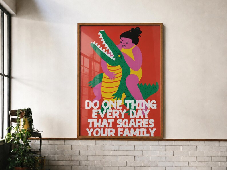 Puede incluir: Un cuadro rectangular enmarcado con fondo rojo que presenta una ilustraci&oacute;n gr&aacute;fica de una persona en traje de ba&ntilde;o amarillo abrazando a un cocodrilo verde. El texto dice: DO ONE THING EVERY DAY THAT SCARES YOUR FAMILY en letras blancas negritas.