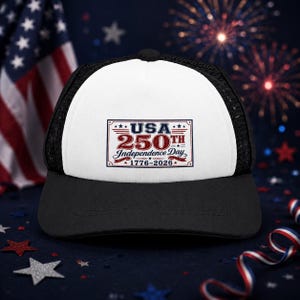 May include: A black and white trucker hat featuring a rectangular graphic on the front panel. The graphic displays the text USA 250TH Independence Day 1776-2026 in red, white, and blue colors, accented with small stars and decorative red ribbon elements.