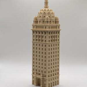 May include: A beige, monochromatic architectural model of a tall skyscraper featuring a central dome, multiple levels of rectangular windows, decorative columns, and a detailed arched entrance at the base, presented as a vertical structure.