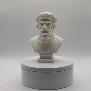 Op de afbeelding: Een wit monochroom borstbeeld van een individu met een baard en een platte pet. Het figuur heeft gedetailleerde gezichtsbeharing, een kledingstuk met een kraag en is gemonteerd op een vierkante voet, gepresenteerd in een neutrale studio.