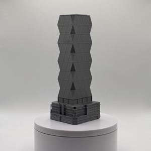 May include: A dark grey architectural model of a skyscraper featuring a rectangular base with detailed window patterns and a tall, faceted tower section with a repeating geometric diamond grid structure that rises vertically from the centre.
