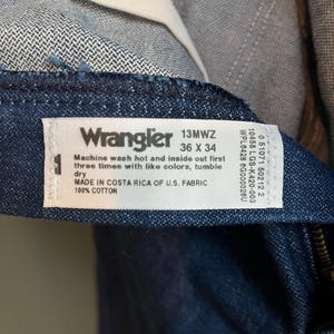 May include: Close-up of a pair of Wrangler jeans. The label reads "Wrangler 13MWZ 36 X 34" and includes washing instructions. The jeans are made in Costa Rica of U.S. fabric and are 100% cotton.
