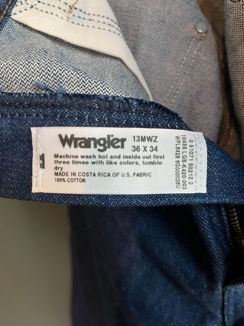 May include: Close-up of a pair of Wrangler jeans. The label reads "Wrangler 13MWZ 36 X 34" and includes washing instructions. The jeans are made in Costa Rica of U.S. fabric and are 100% cotton.
