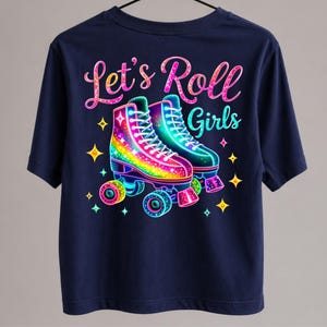 Może przedstawiać: Granatowa koszulka z kolorową grafiką dwóch rolek i napisem "Let's Roll Girls". Rolki są ozdobione tęczowymi i neonowymi kolorami, otoczone gwiazdami.