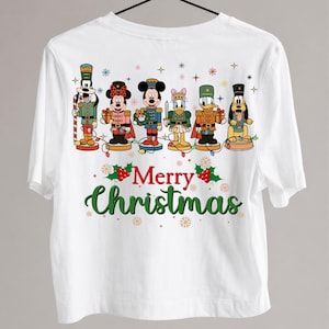 May include: A white t-shirt featuring a graphic of six Disney characters dressed as nutcrackers, including Goofy, Minnie, Mickey, Daisy, Donald, and Pluto. Below the characters, the text Merry Christmas is printed in red and green script.
