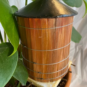 May include: A miniature wooden water tower with a black painted roof. The tower is made of thin wooden slats and has a series of metal bands around it.