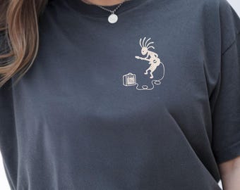 Könnte beinhalten: Ein dunkel anthrazitfarbenes T-Shirt mit einer kleinen, hellen Grafik auf der linken Brust. Das Design zeigt eine stilisierte Figur mit stacheligen Haaren, die eine E-Gitarre spielt und per Kabel mit einem kleinen Verstärker am Boden verbunden ist.