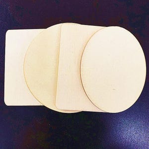 Könnte beinhalten: Eine Ansammlung von vier unbehandelten, hellen Holzformen, bestehend aus zwei Quadraten mit abgerundeten Ecken und zwei Kreisen. Die Holzteile sind überlappend angeordnet und zeigen eine glatte, flache Oberfläche mit einer natürlichen Maserung.