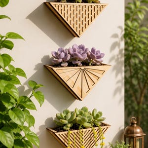 May include: Three triangular wooden wall planters mounted vertically. The top planter has a diamond grid pattern, the middle has a sunburst design, and the bottom has vertical slats. Each contains green or purple succulents, with yellow flowers.