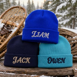 Può includere: Tre berretti in maglia blu reale, blu navy e verde acqua. Il berretto blu reale presenta il nome LIAM ricamato in argento. Il berretto blu navy presenta il nome JACK in color cuoio, e il berretto verde acqua presenta il nome OWEN in blu scuro.