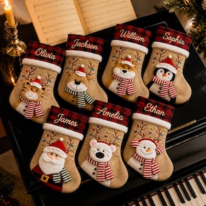 May include: Seven Christmas stockings made of tan burlap with red and black buffalo plaid cuffs. Each cuff features a white embroidered name: Olivia, Jackson, William, Sophia, James, Amelia, and Ethan. Each stocking displays a plush holiday character.