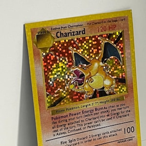 May include: A holographic Charizard trading card featuring the orange dragon-like creature with wings spread. The card displays 120 HP, the text Flame Pokémon, Length: 5' 7", Weight: 200 lbs., and the Pokémon Power: Energy Burn ability text.