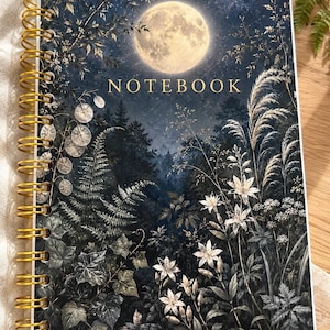 May include: A spiral-bound notebook featuring a dark, nocturnal forest scene with a large, glowing full moon in the night sky. The cover displays the word NOTEBOOK in gold lettering, surrounded by detailed illustrations of ferns, ivy, and wildflowers.