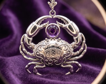 Op de afbeelding: Een zilverkleurige metalen hanger in de vorm van een krab, met een ronde paarse edelsteen boven het schild. Het schild is gegraveerd met drie tarotkaarten met zon-, maan- en stersymbolen, omringd door gedetailleerde, zwierige patronen.